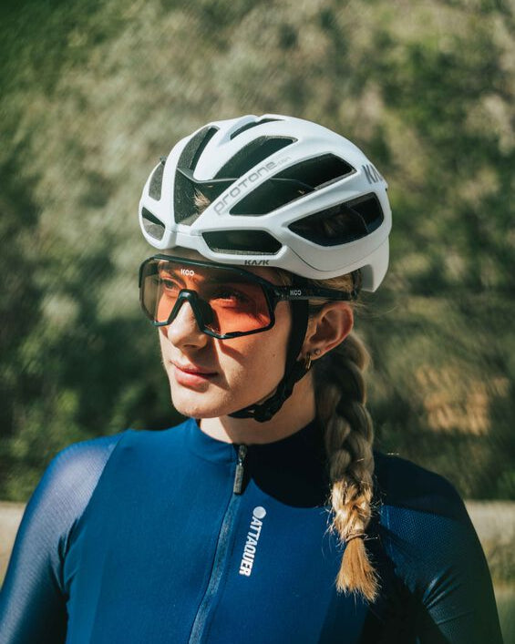 Person wearing a white helmet and blue cycling outfit with sunglasses outdoors.