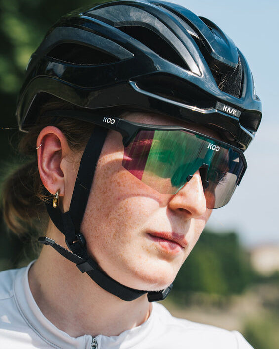 Person wearing a black helmet and sunglasses with a blurred outdoor background