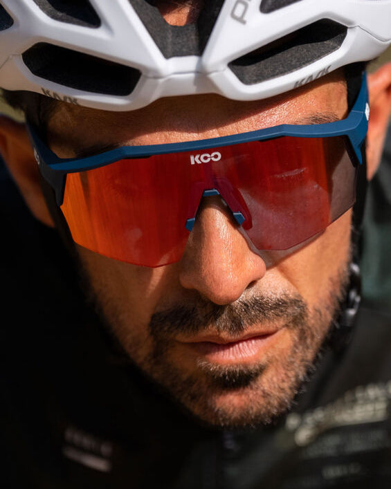 Person wearing a white bicycle helmet and red sunglasses with a brand logo.