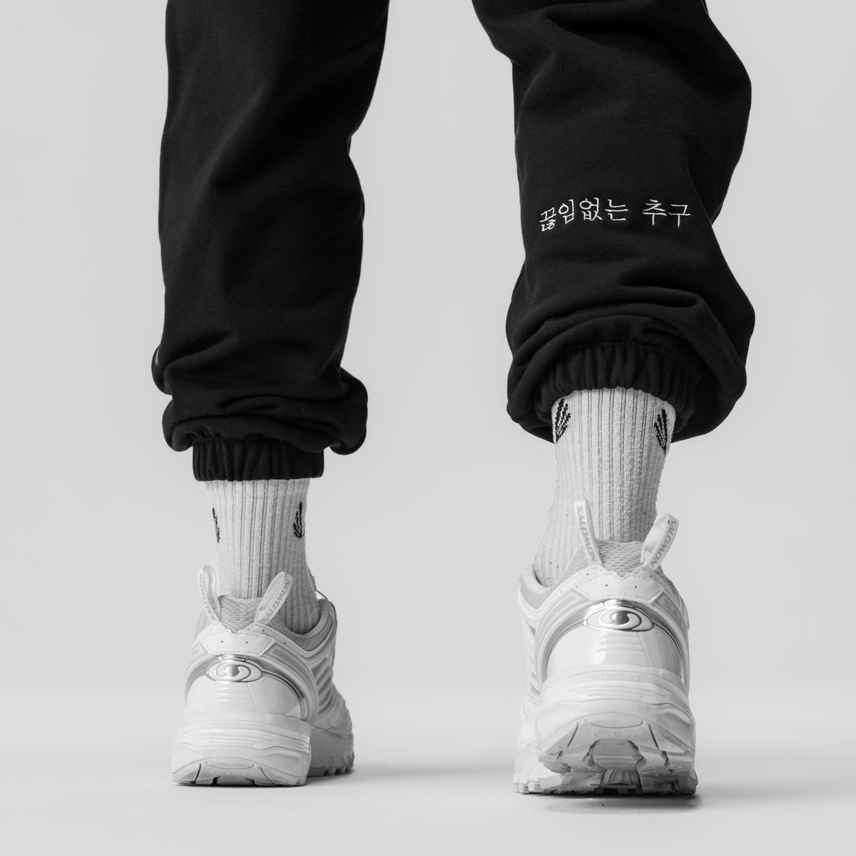 Black Tech-Terry oversized sweats with Korean text embroidered on cuff, worn with white socks and sneakers, back view