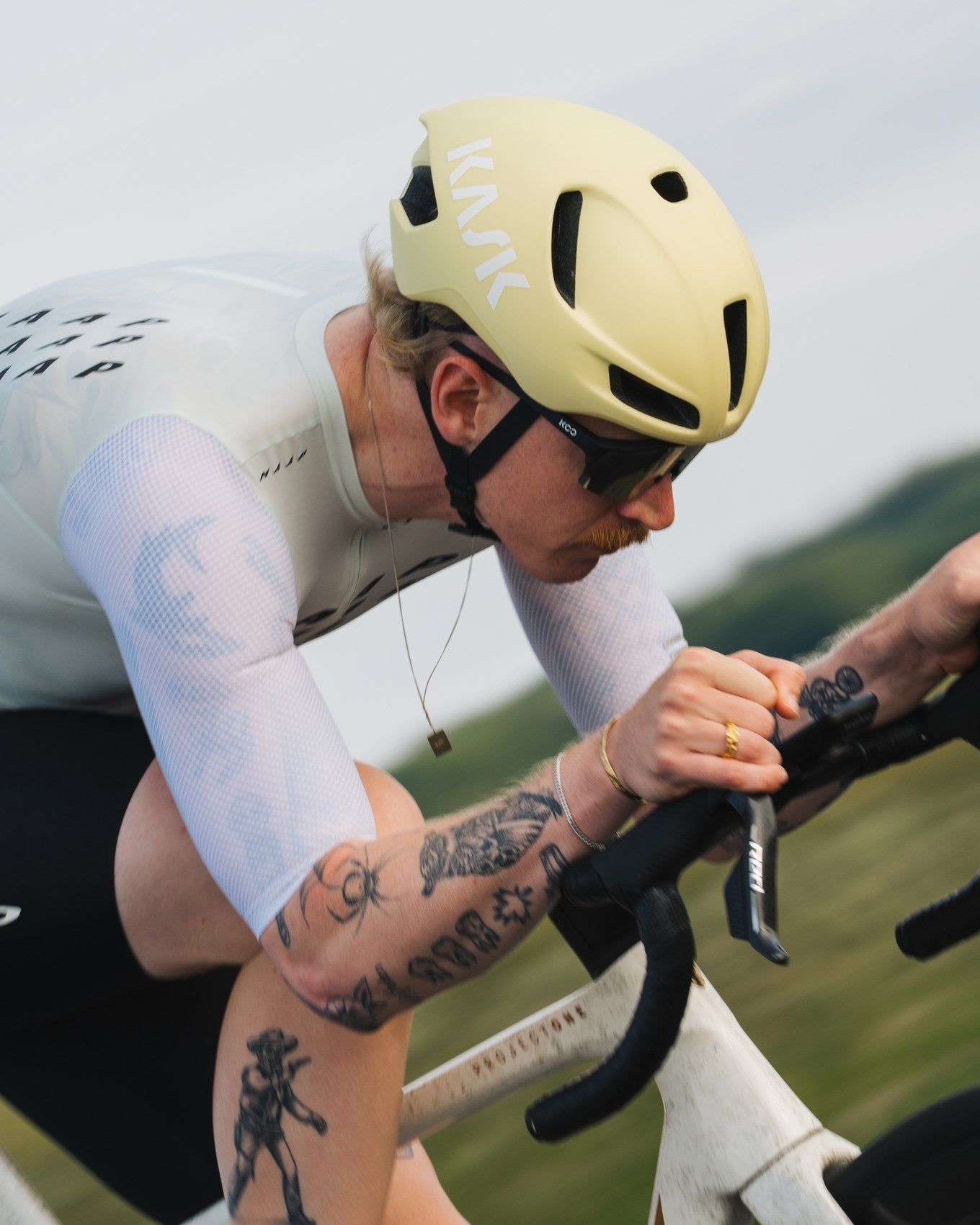 Cyclist in a white outfit and beige helmet riding a bicycle with a scenic background.