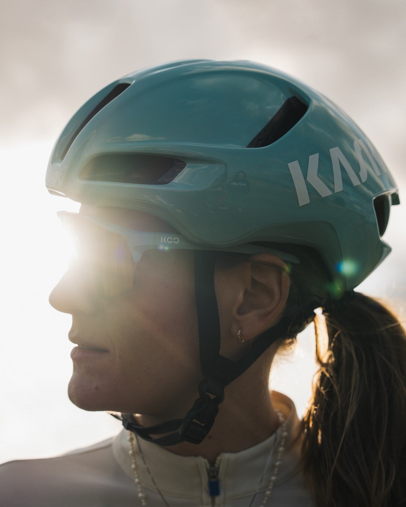Person wearing a teal helmet with 'Kali' branding against a blurred background