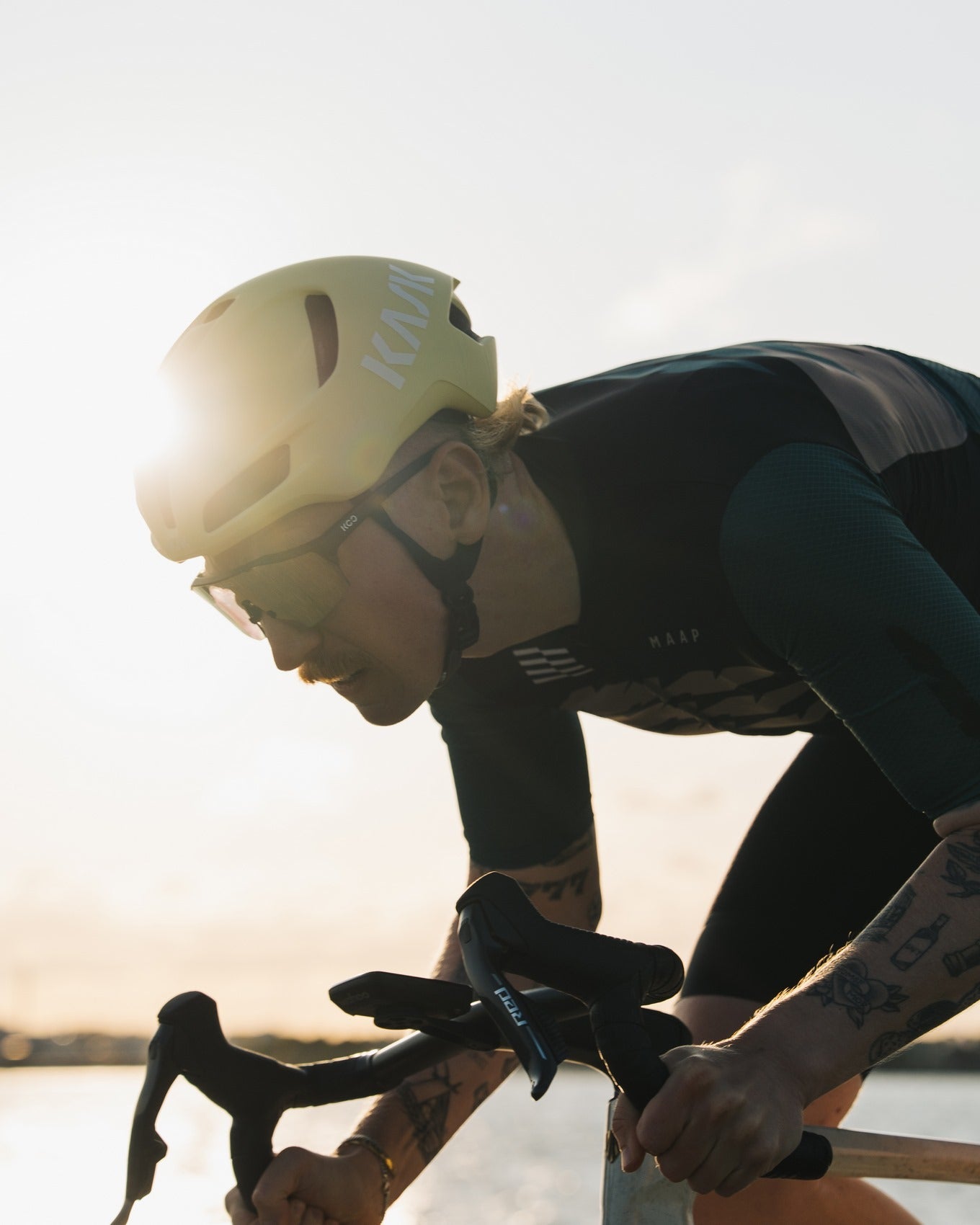 Cyclist in a wetsuit and helmet riding a bike with a sunset in the background