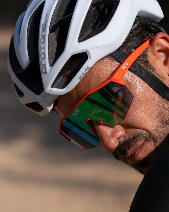 Person wearing a white bicycle helmet and orange sunglasses with a blurred background
