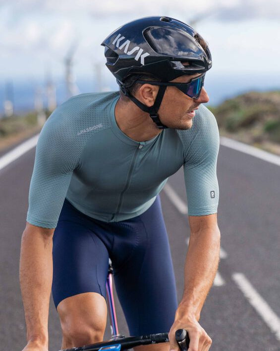 Cyclist in a blue and black cycling outfit on a road with a scenic background