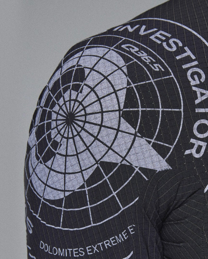 Close-up of a black ribbed athletic jacket showing the shoulder and upper back with a large white circular 'INVESTIGATOR' graphic and polar grid design.